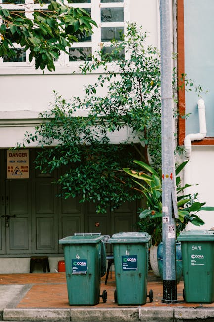 A wooden two-wheeled cart with large, spoked wheels and metal chains securing its sides is parked on a brick-paved street in front of a brick building with two white-framed windows, each with window b
