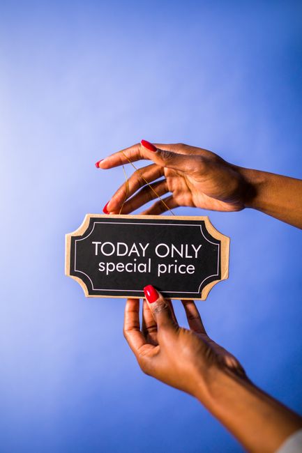 A pair of hands with neatly manicured nails painted red are holding a small black and beige price tag with gold accents, displaying the words 'TODAY ONLY special price' against a plain blue background