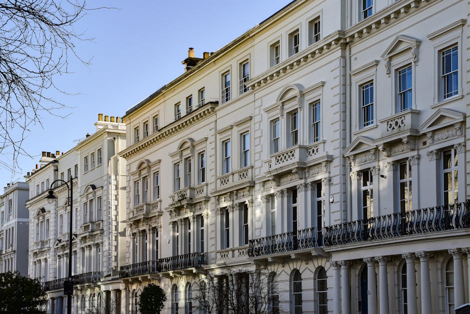 A row of Victorian-style terraced houses with multi-pane sash windows and decorative mouldings, painted in varying pastel shades including light blue, turquoise, beige, black, and bright green. The bu